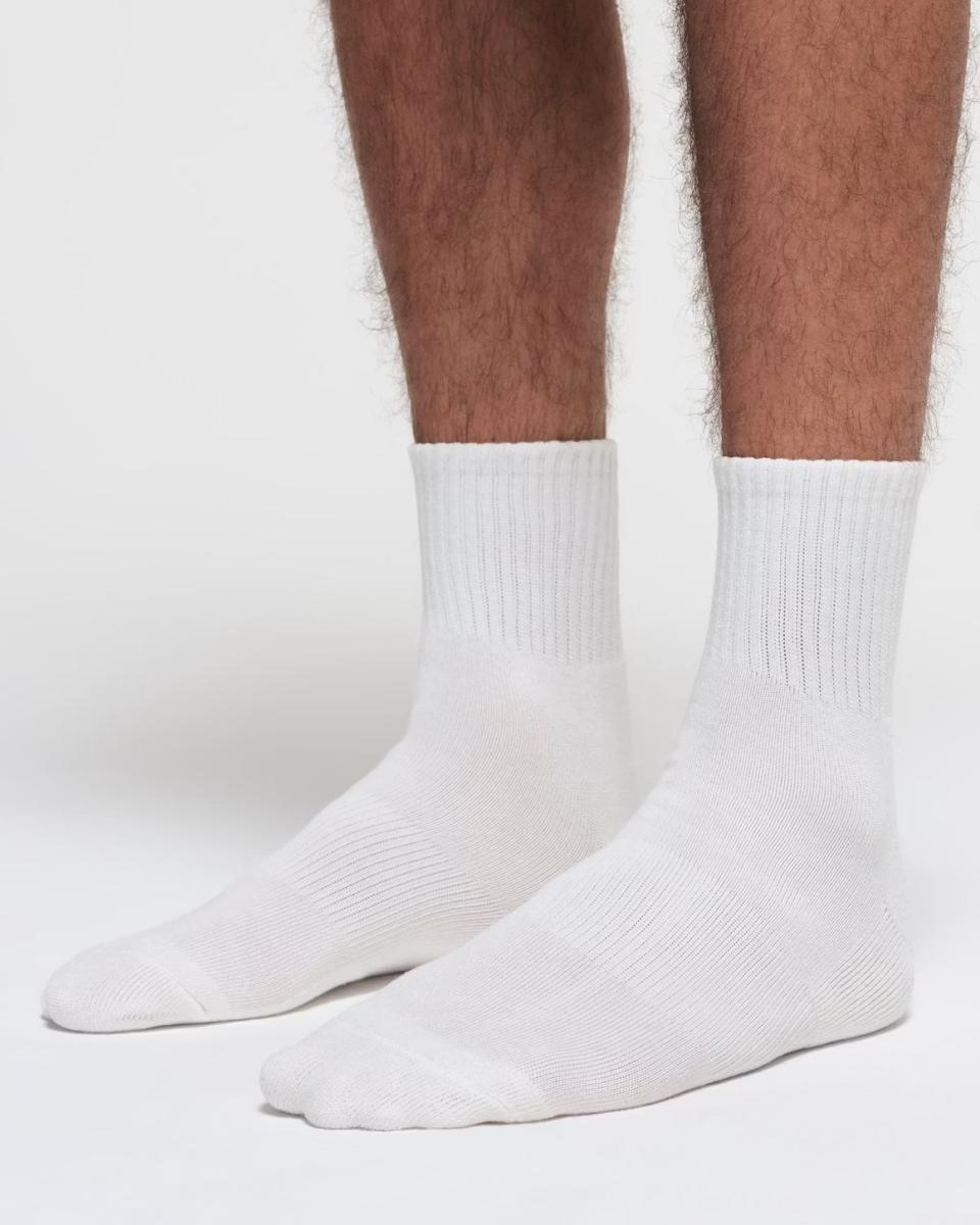 A MODEL POSES WEARING SKIMS MENS LOUNGE SOCKS